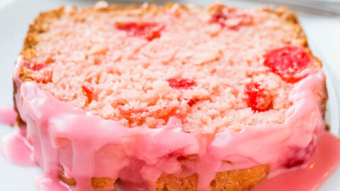 A slice of pink frosted cake with visible chunks of fruit on a white plate.