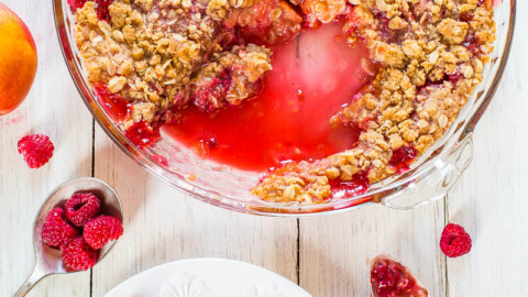 A freshly baked peach and raspberry crisp with a scoop served on a plate.