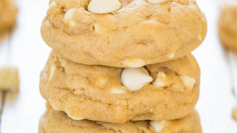 A stack of white chocolate chip cookies on a light wooden surface.