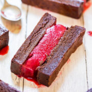 A chocolate dessert with a bright red jelly filling on a wooden surface.