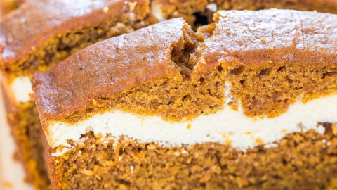 A close-up image of a sliced pumpkin cream cheese loaf on a wooden surface.