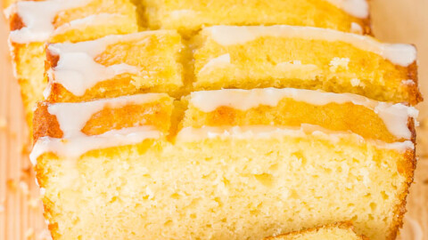 Sliced lemon loaf cake with white glaze on a wooden surface.