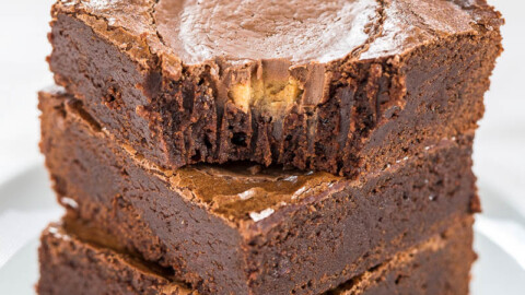 Three stacked chocolate brownies with a glossy crust on a white plate.