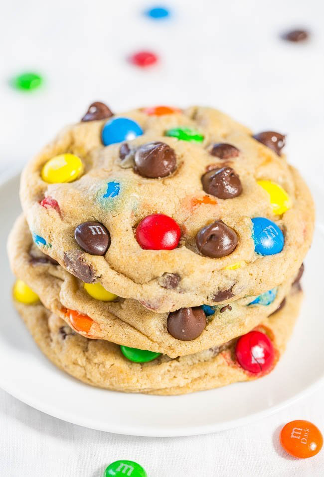 A stack of three colorful candy and chocolate chip cookies on a white plate, with scattered candies around.