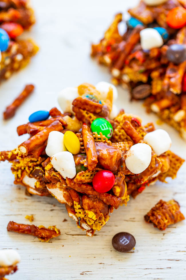 A snack mix bar with pretzels, marshmallows, colorful candies, and cereal pieces on a white surface.