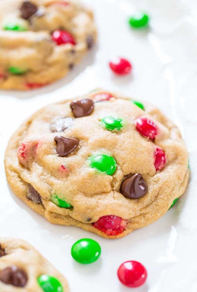 A cookie with red and green candies and chocolate chips on a white surface.