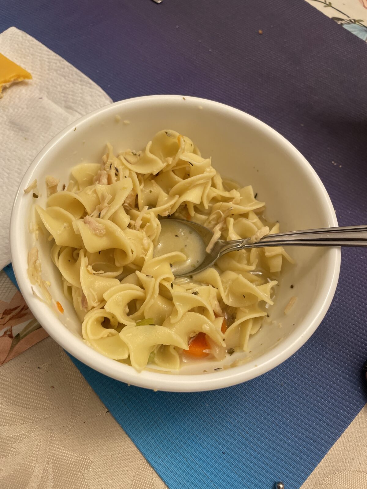 A bowl of pasta with vegetables and a creamy sauce, with a spoon resting inside.