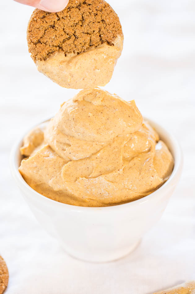 A person dips a cookie into a bowl of creamy, light-brown pumpkin dip.