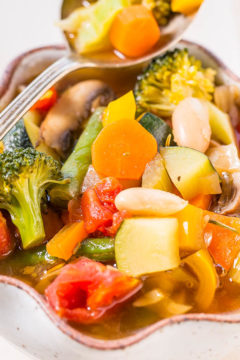 A colorful bowl of vegetable soup with broccoli, carrots, tomatoes, and mushrooms.