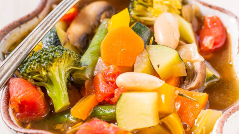 A colorful bowl of vegetable soup with broccoli, carrots, tomatoes, and mushrooms.