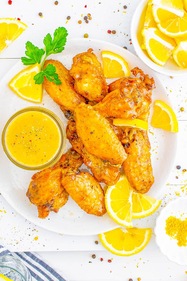 Plate of fried chicken wings with lemon slices and a small bowl of yellow dipping sauce, garnished with parsley.