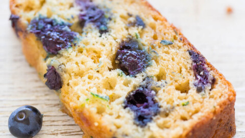 A slice of blueberry loaf cake with whole blueberries scattered around.