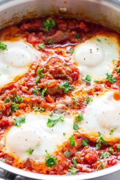 A skillet containing shakshuka, a dish of poached eggs in a tomato and pepper sauce garnished with fresh herbs.