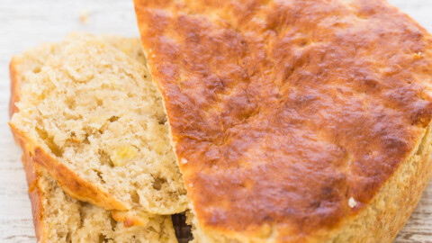 A loaf of freshly baked bread with one slice partly cut on a wooden table.