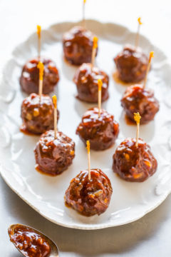 A plate of glazed meatballs with toothpicks served as appetizers.