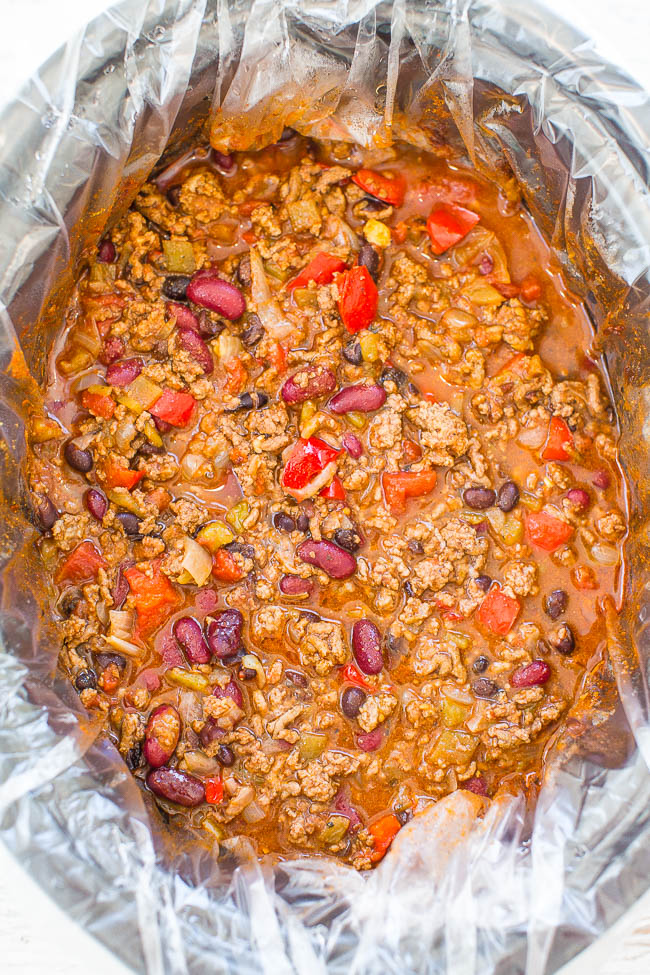 A pot of beef chili with beans and vegetables, cooking in a slow cooker lined with a disposable bag.