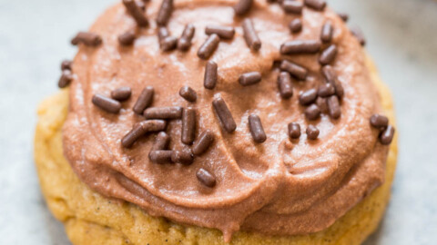 A freshly baked cookie topped with chocolate frosting and sprinkles.