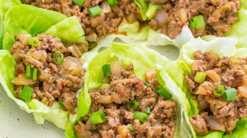 A plate of lettuce wraps filled with savory minced meat and diced vegetables, garnished with sliced green onions.