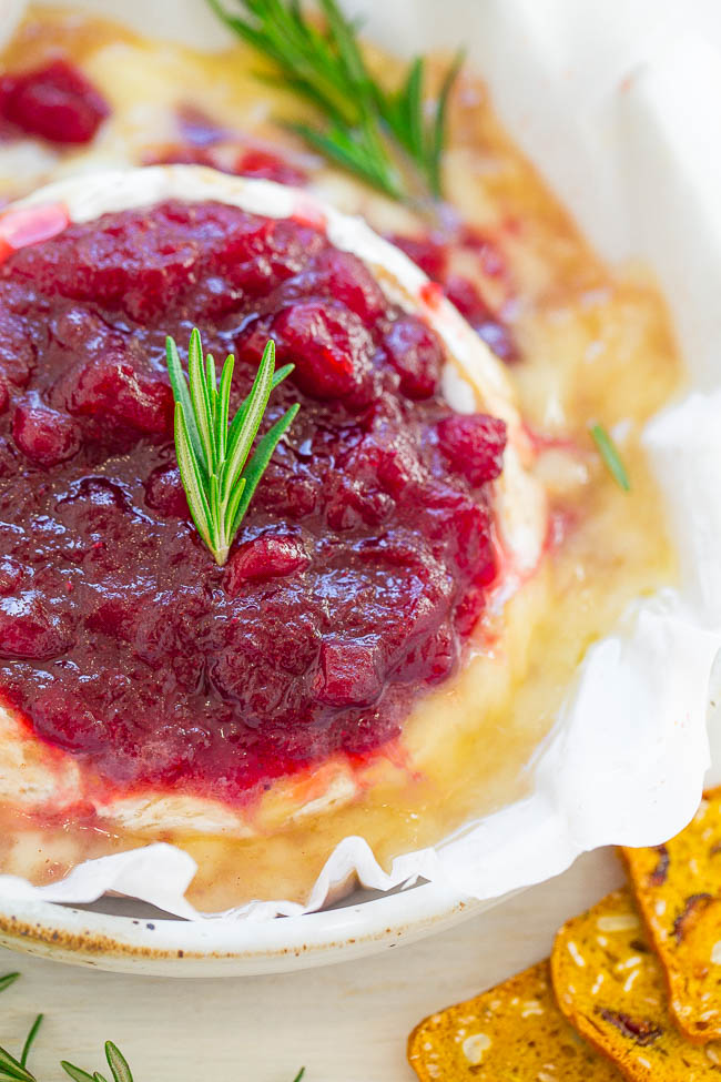 Baked brie with a cranberry topping garnished with a sprig of rosemary.