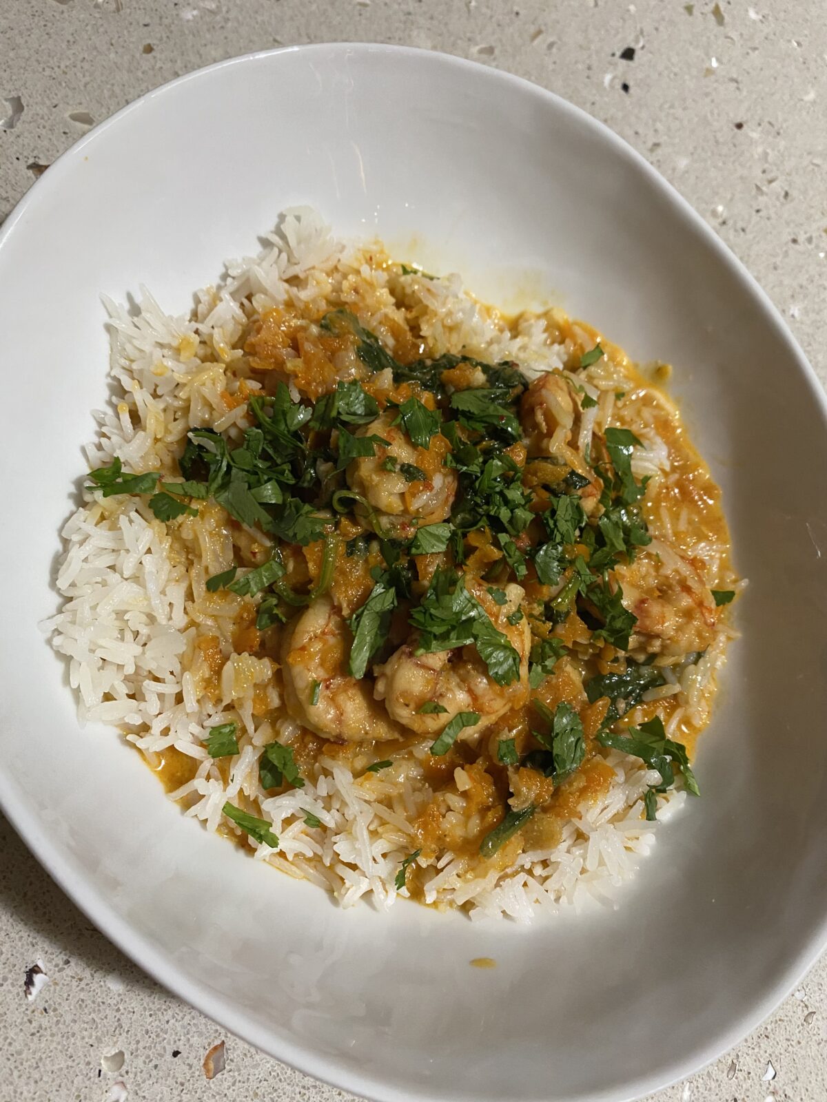 A bowl of white rice topped with shrimp in a sauce and garnished with chopped herbs.