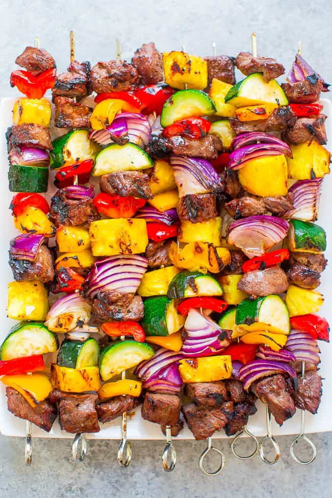 Colorful grilled vegetable and beef kabobs on a white plate.