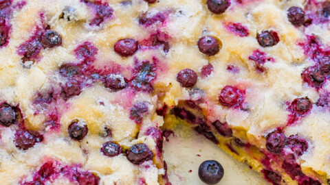 A freshly baked blueberry cake in a glass dish, with whole blueberries scattered around.