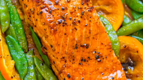 Grilled salmon fillet with snap peas and sliced carrots on aluminum foil.