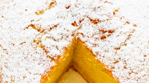 A freshly baked sponge cake with a dusting of powdered sugar and one slice removed.