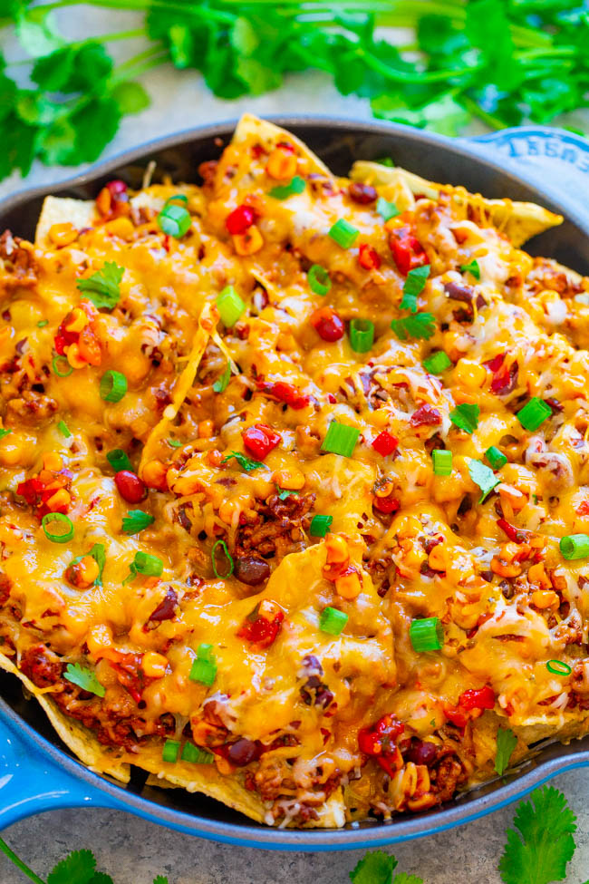 A skillet filled with baked cheesy nachos garnished with green onions.