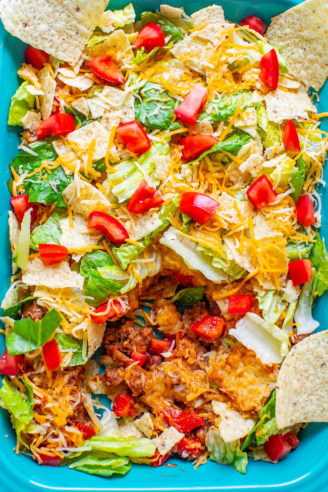 A close-up of a taco salad with lettuce, tomatoes, shredded cheese, ground meat, and tortilla chips in a blue dish.