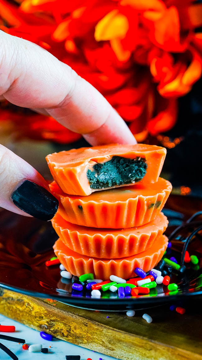 Hand holding a half-eaten orange chocolate cup stacked on two others, surrounded by colorful sprinkles.