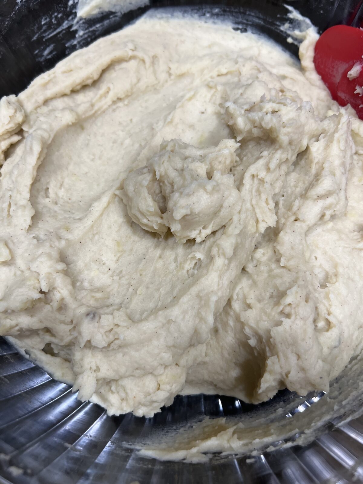 Close-up of mashed potato mixture in a mixing bowl with a red spatula.