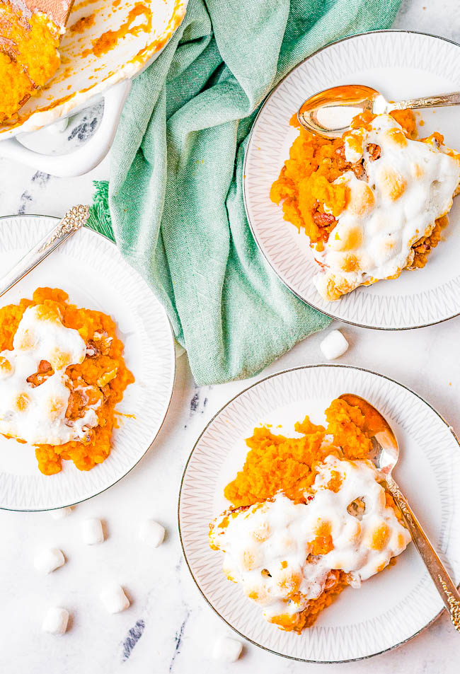 Three plates of sweet potato casserole topped with melted marshmallows. A green cloth is placed beside the plates, and a few marshmallows are scattered on the white marble surface.