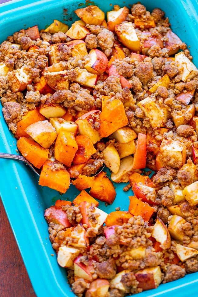 A blue baking dish filled with a mixed fruit crisp, featuring chunks of apples, pears, and peaches topped with a streusel crumble.