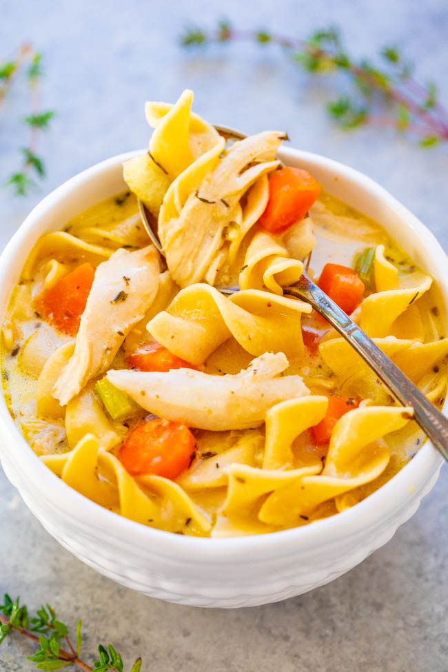 A bowl of chicken noodle soup with vegetables and herbs.