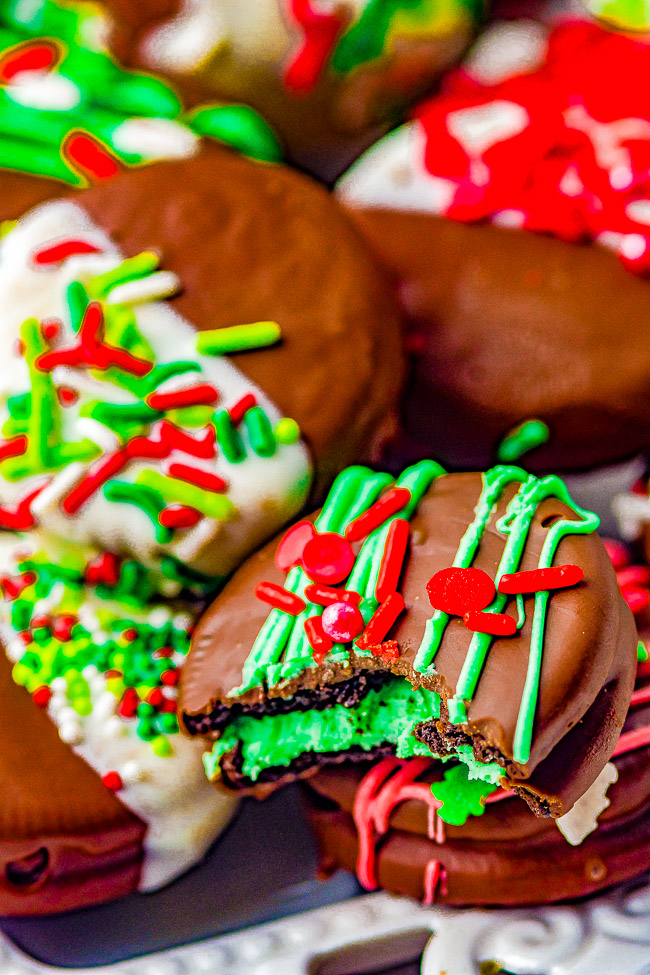 Festively decorated chocolate-covered cookies with green filling, topped with red and green sprinkles and icing, arranged on a surface.