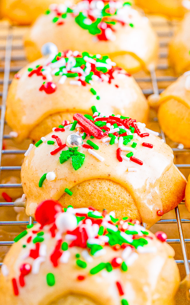 Close-up of cookies with white icing and red, green, and white sprinkles, cooling on a wire rack.