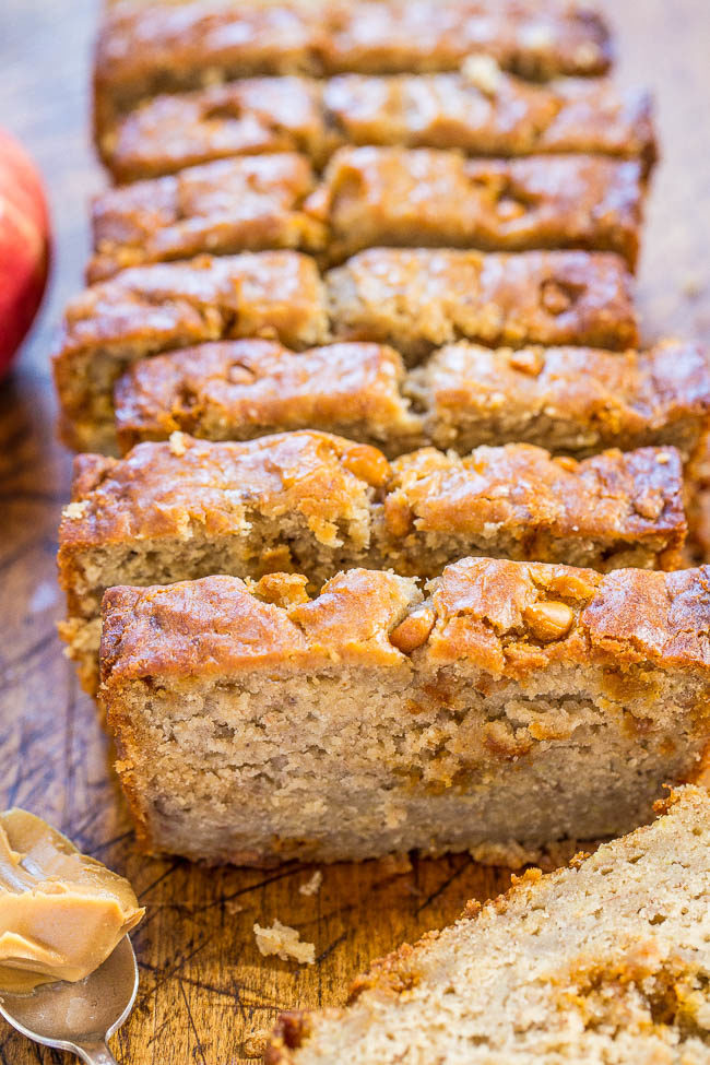 Sliced loaf of peanut butter banana bread on a wooden surface, with a spoonful of peanut butter nearby.