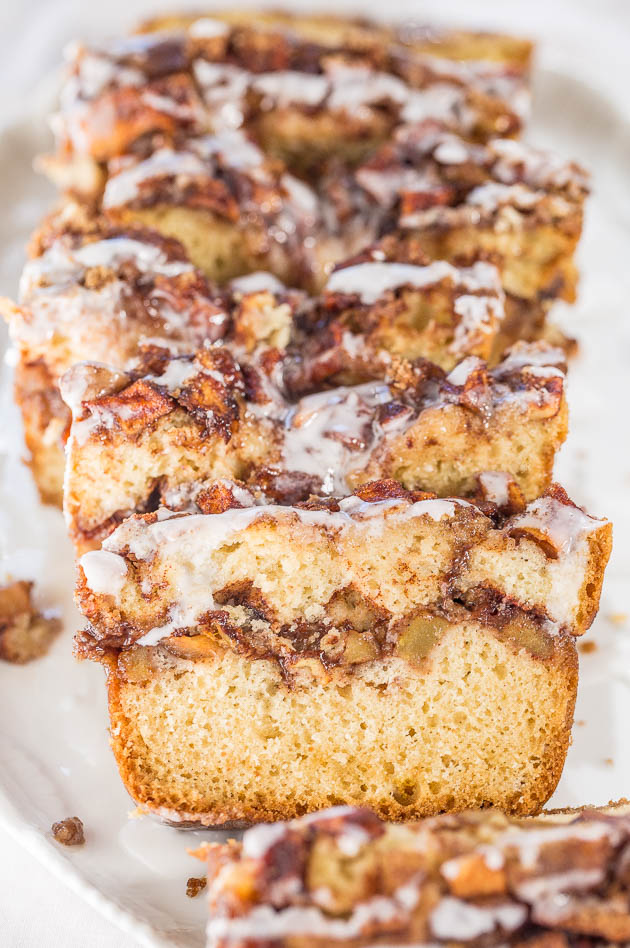 Sliced loaf of cinnamon swirl bread topped with a glaze, arranged on a white plate.