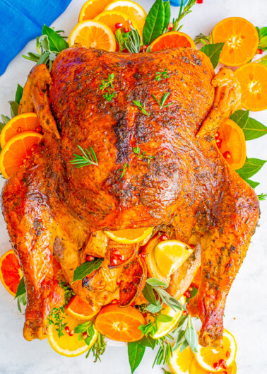 Roasted chicken garnished with slices of orange and herbs on a serving platter.