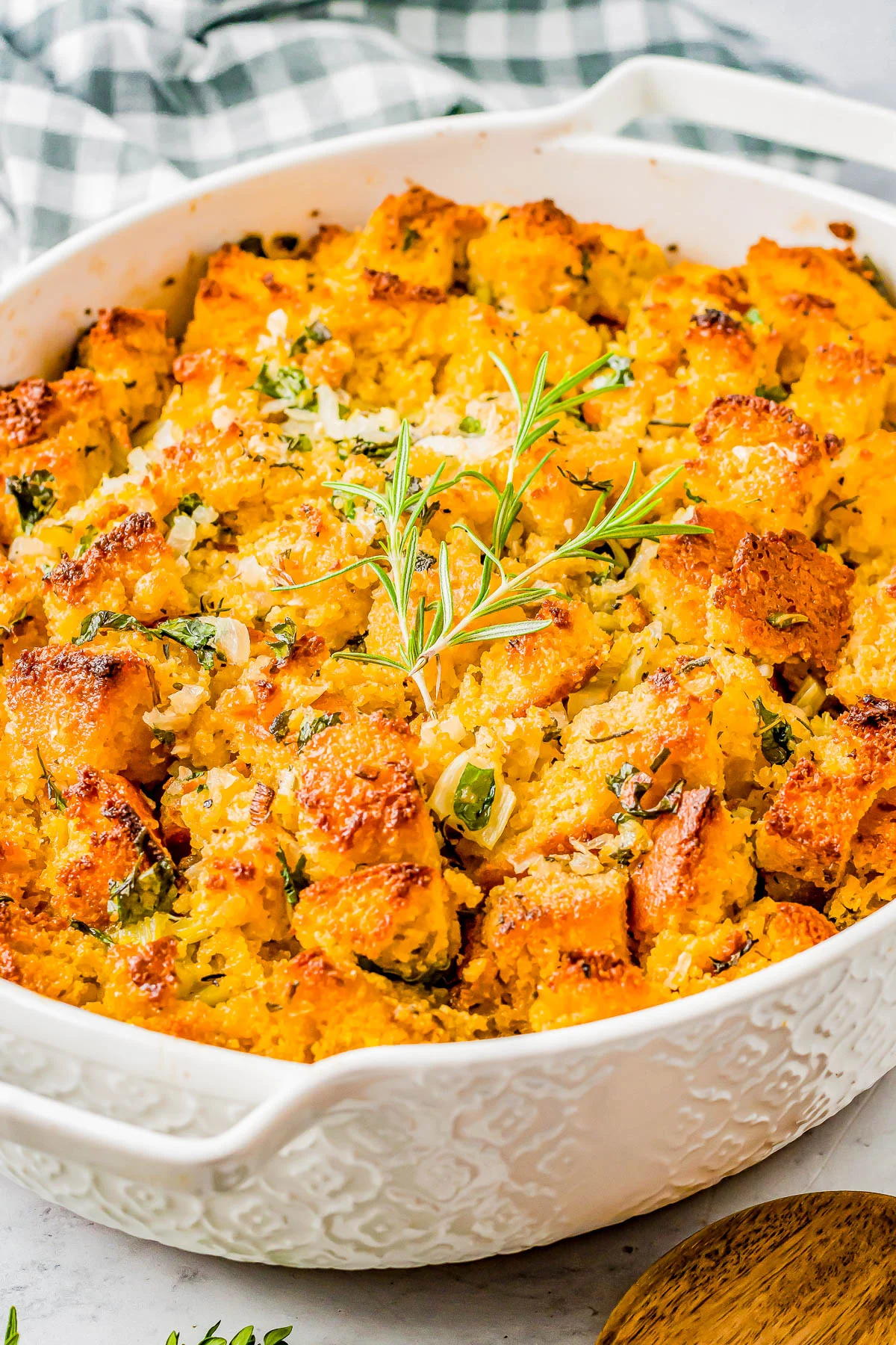 A baked dish of golden-brown stuffing garnished with fresh rosemary in a white casserole dish.