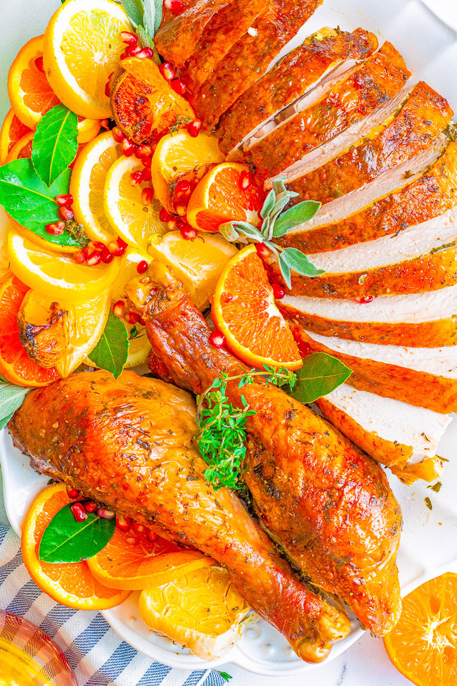 A platter with roasted turkey slices and drumsticks garnished with orange slices, pomegranate seeds, and fresh herbs.