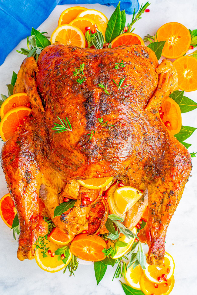 Roasted turkey garnished with herbs, lemon, and orange slices on a white surface.