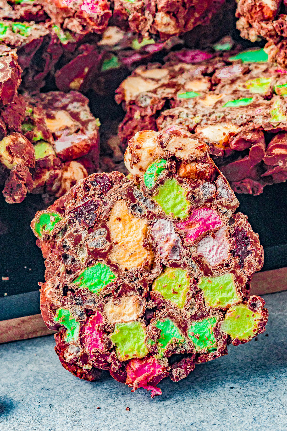 Close-up of colorful rocky road candy bars with visible chunks of marshmallows and chocolate on a gray surface.