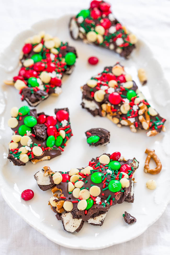 A plate of festive chocolate bark topped with red and green candies, white chocolate chips, pretzels, and sprinkles.