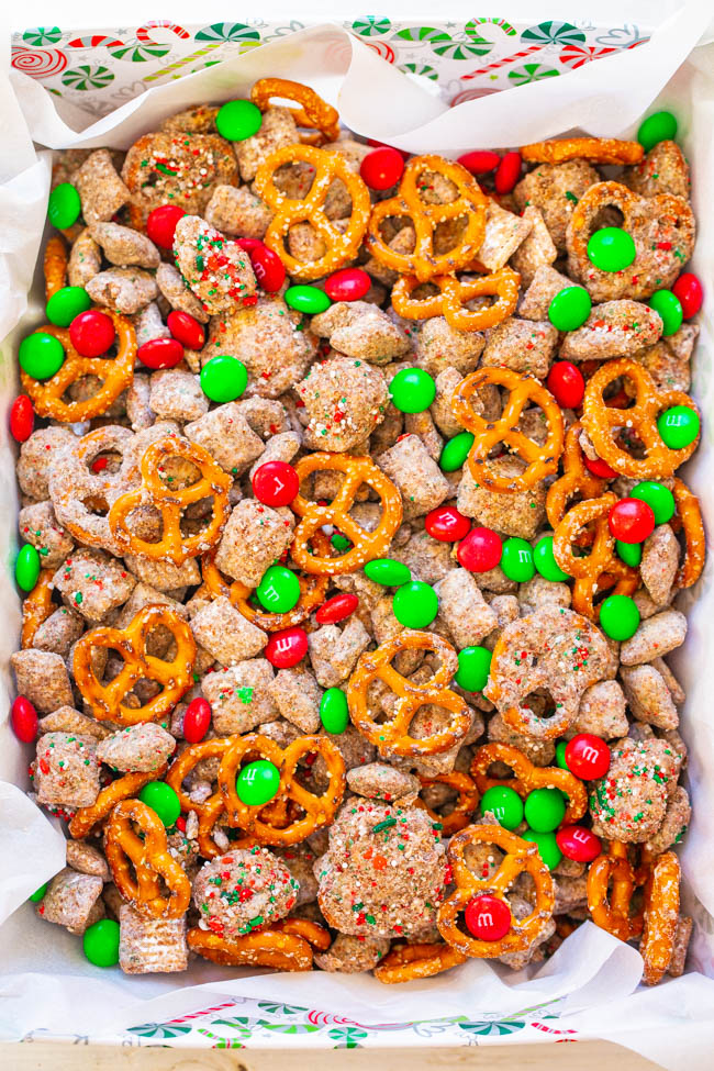 A festive mix of pretzels, red and green candies, cereal squares, and nuts in a tray lined with white paper.