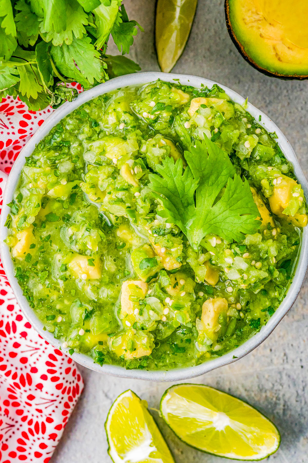 A bowl of fresh avocado salsa garnished with cilantro, surrounded by lime wedges and an avocado half.