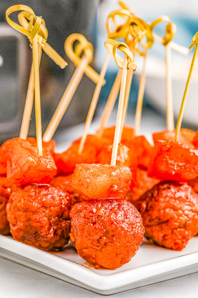 Skewered meatballs with pineapple chunks, glazed with a reddish sauce, arranged on a white square plate.