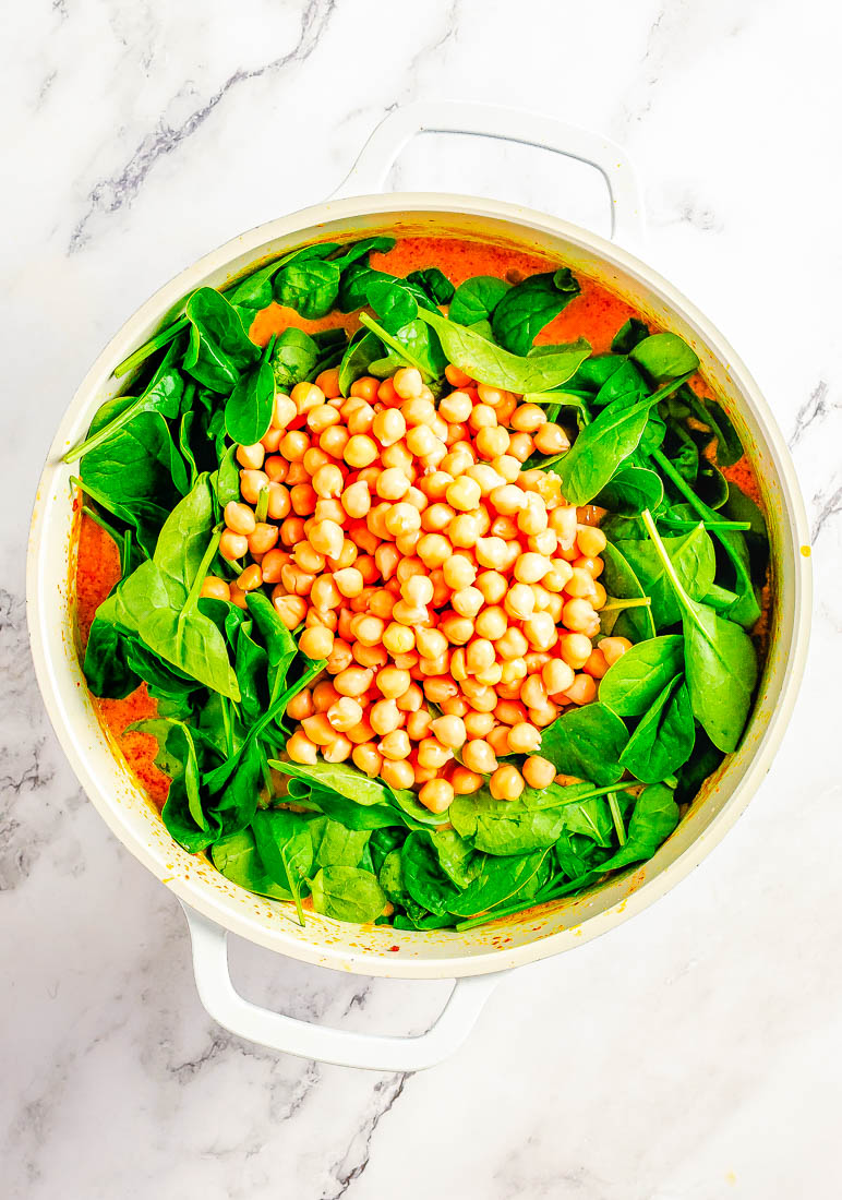 A pot of chickpeas and spinach on a marbled surface.