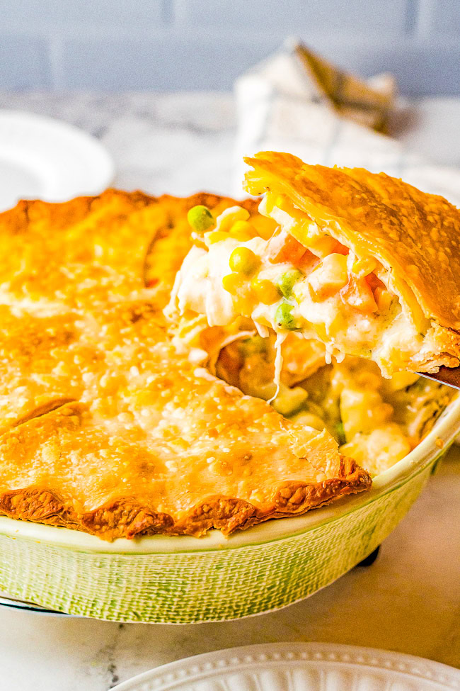 A golden-brown pot pie with a flaky crust being served, showing creamy filling with peas, carrots, and other vegetables.